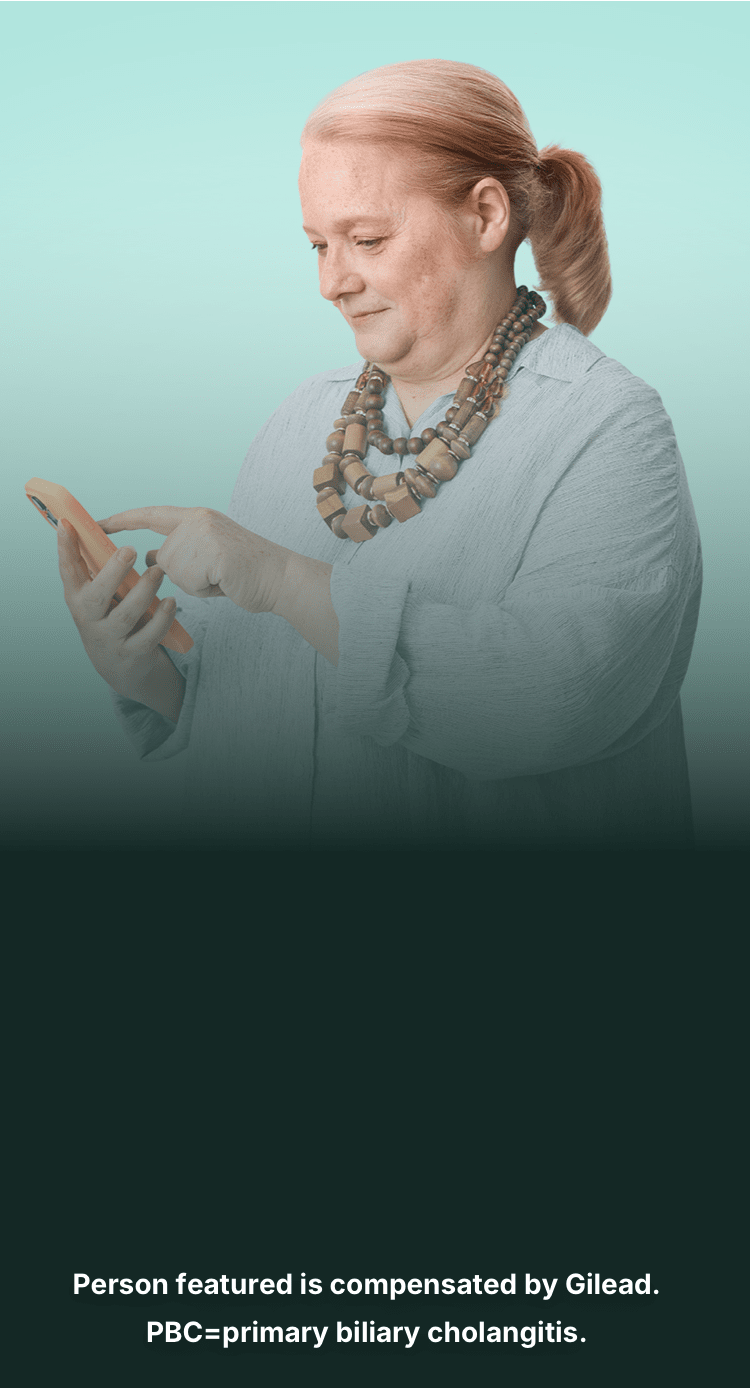 Wendy, a woman with PBC, reading her phone standing in front of a teal background